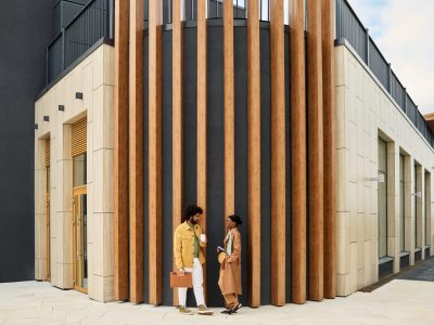 Two people having conversation outside contemporary structure with wooden accents and tall vertical elements. Modern design and clean lines define the architecture