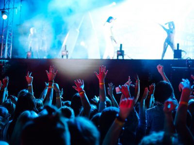 ?rowd with raised hands at music festival. Fans enjoying rock concert with light show clapping hands